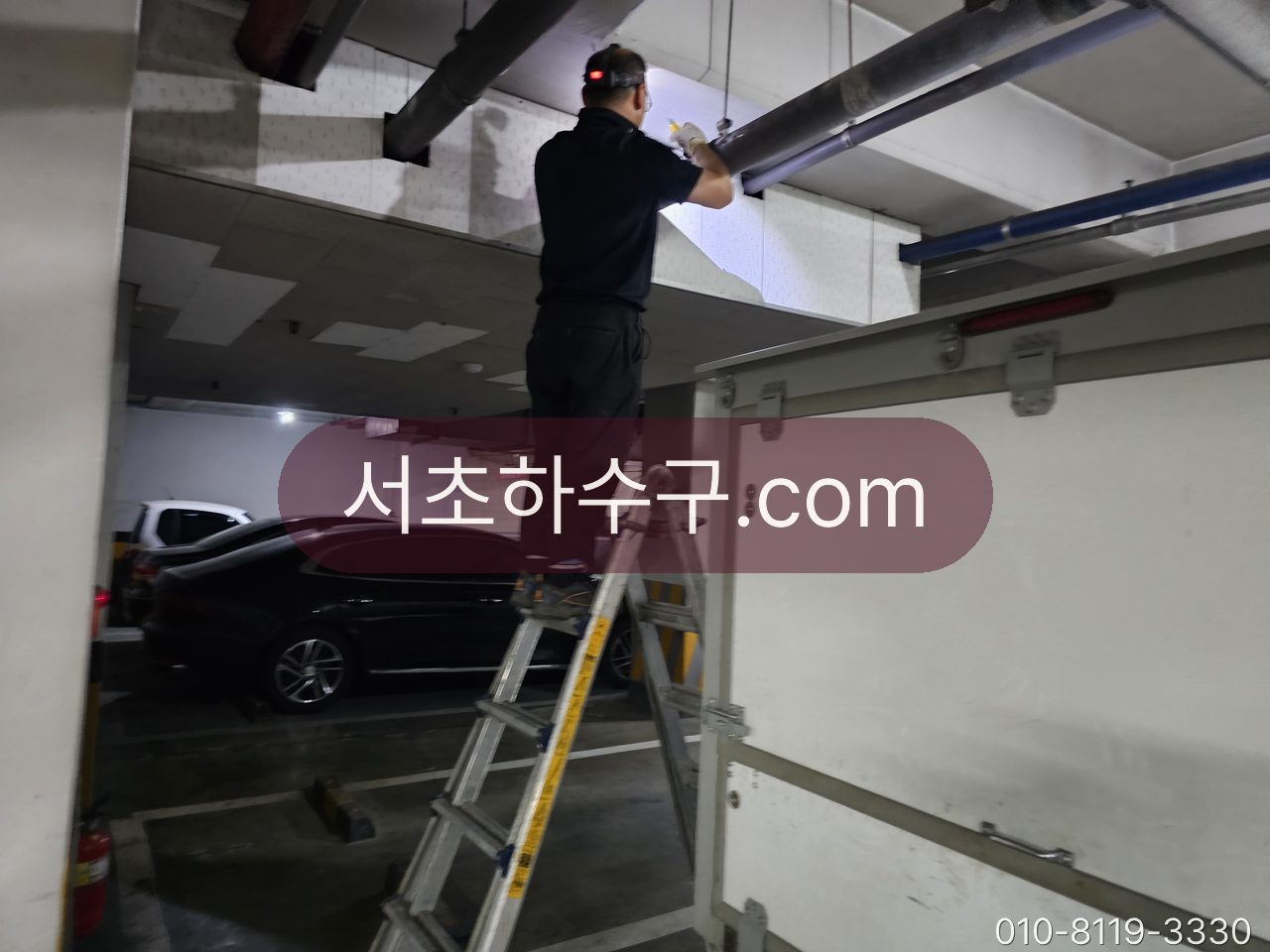 지하주차장 천장의 횡주관 소제구를 사다리 위에서 열고 작업하는 장면