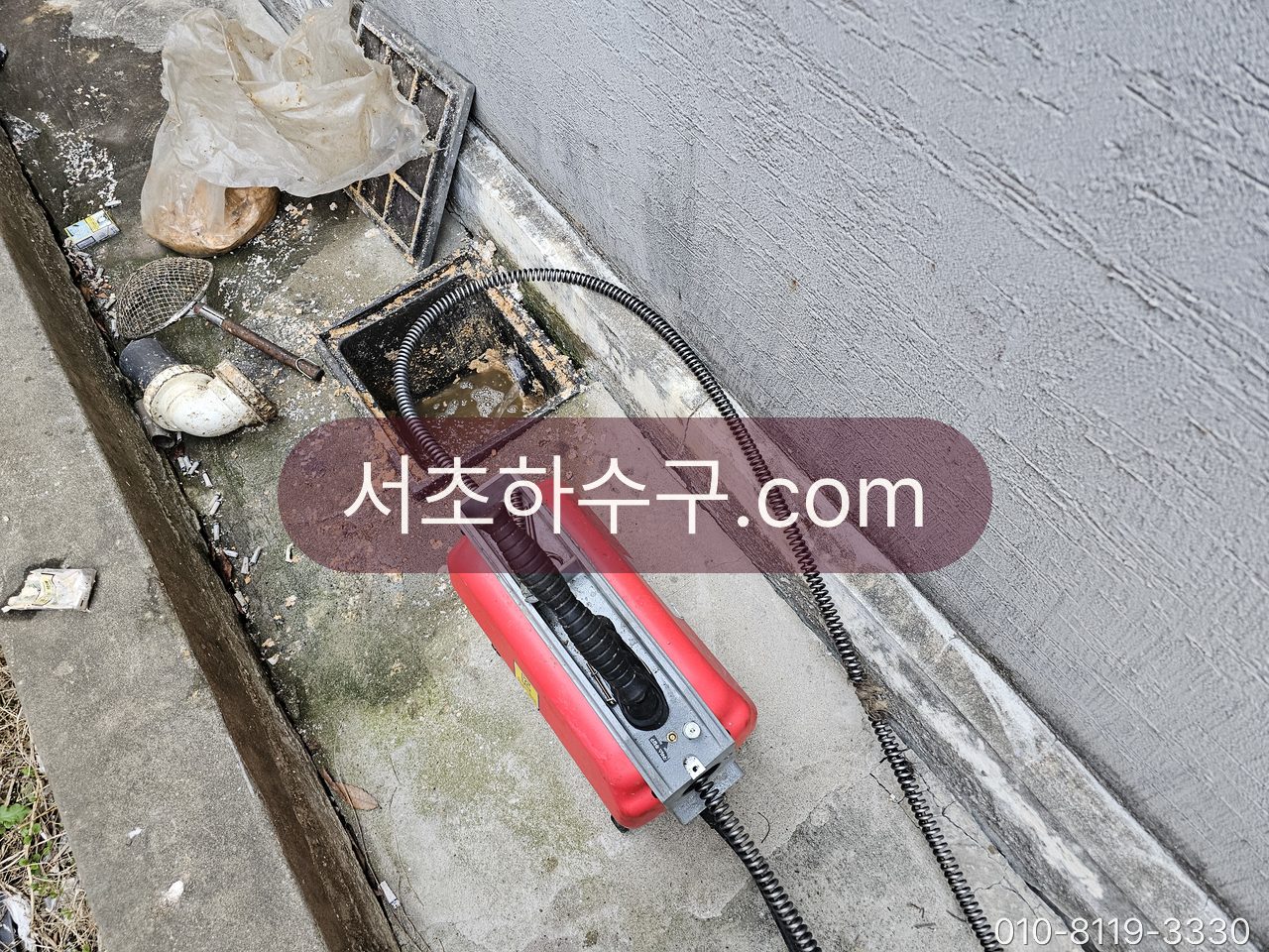 건물 옥상 통로의 배수구 드레인에 쌓인 이물을 관통 장비로 걷어내는 장면